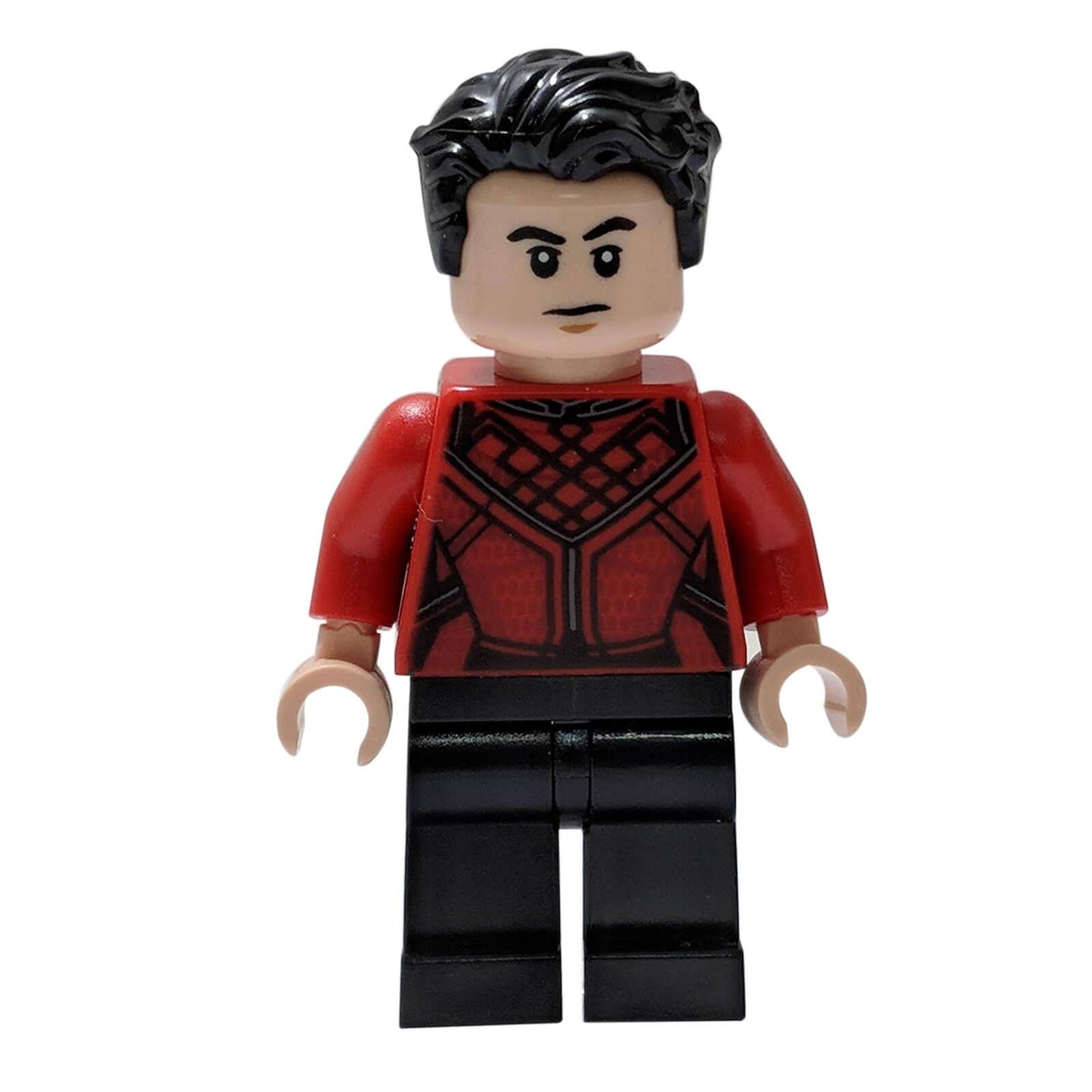Minifigurka LEGO® Shang-Chiho, s černými vlnitými vlasy, světlou nugátovou hlavou s odhodlaným výrazem a tenkým knírkem, červeným trupem s propracovaným černým vzorem, červenými pažemi, světlými nugátovými rukama a černými nohami, stojící na bílém pozadí.