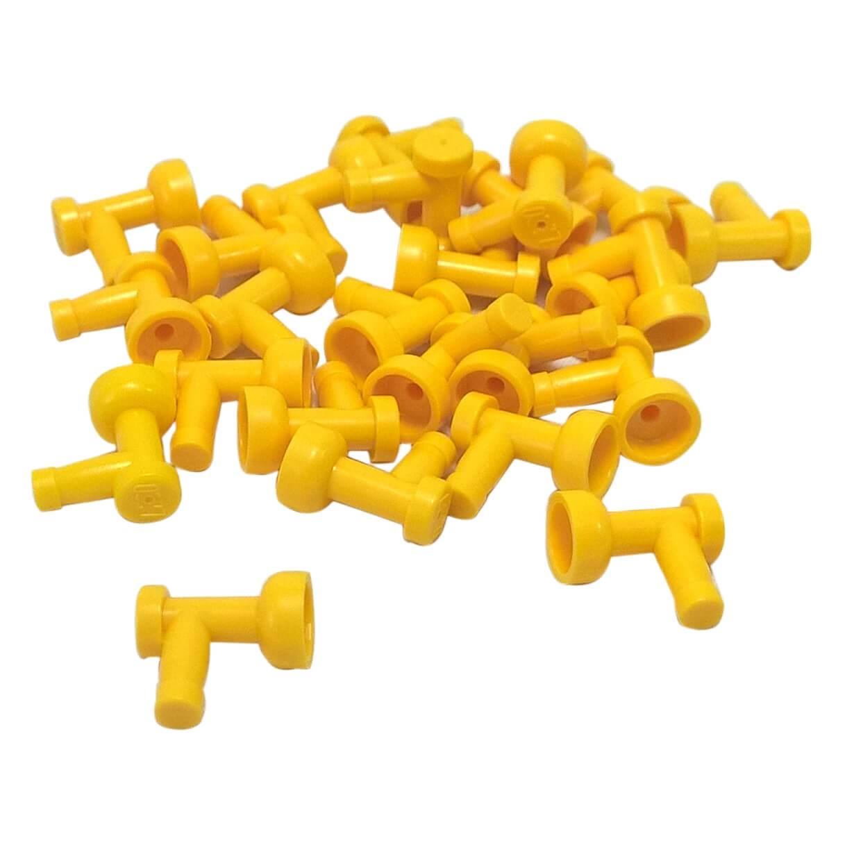 A pile of numerous bright yellow LEGO Part 4599b (Tap 1 x 1 without Hole in End) pieces scattered against a white background, showing their T-shape with a flared cup end.