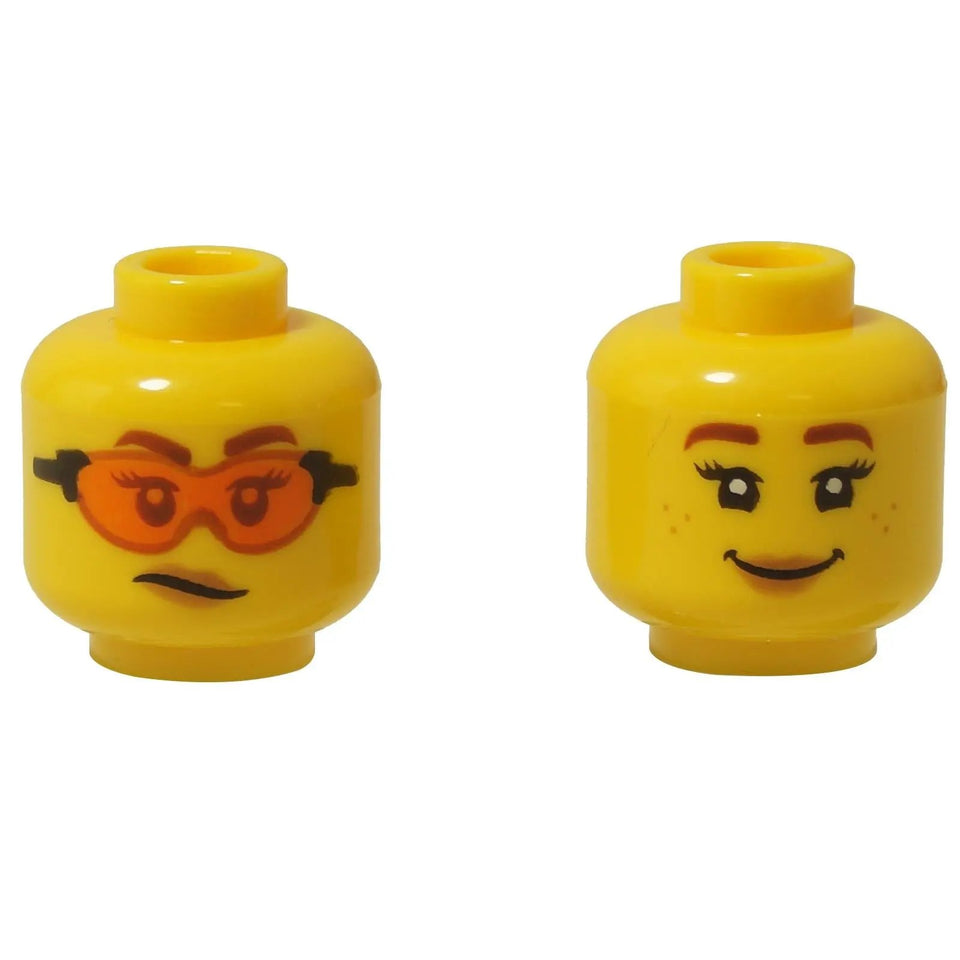 A dual-sided yellow LEGO® minifigure head (3626pb2761) with a scowl and orange goggles on one side, and a friendly smile with freckles on the other.