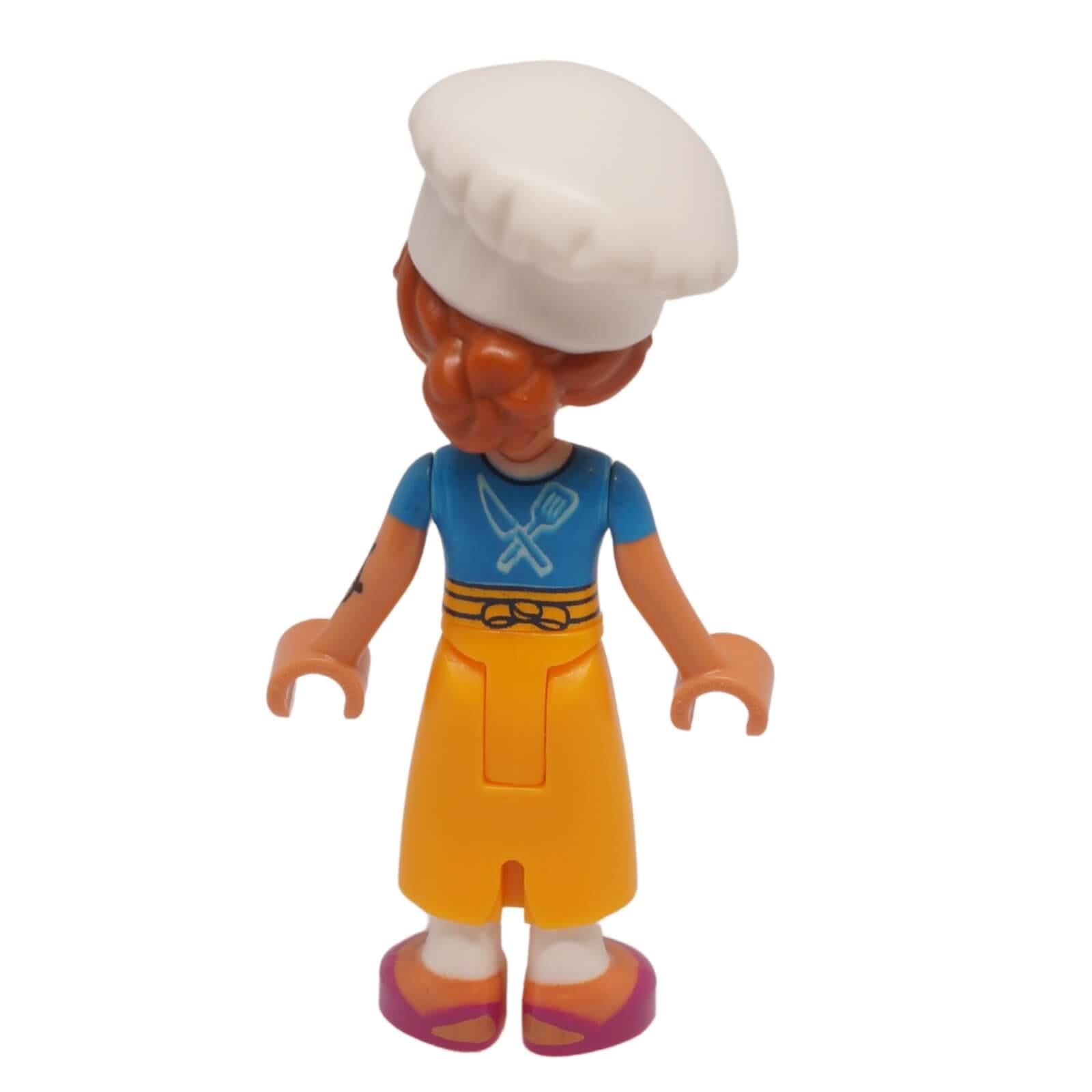 Vista posterior de la minimuñeca de Chef Marta Friends con gorro de chef blanco, top azul y falda naranja
