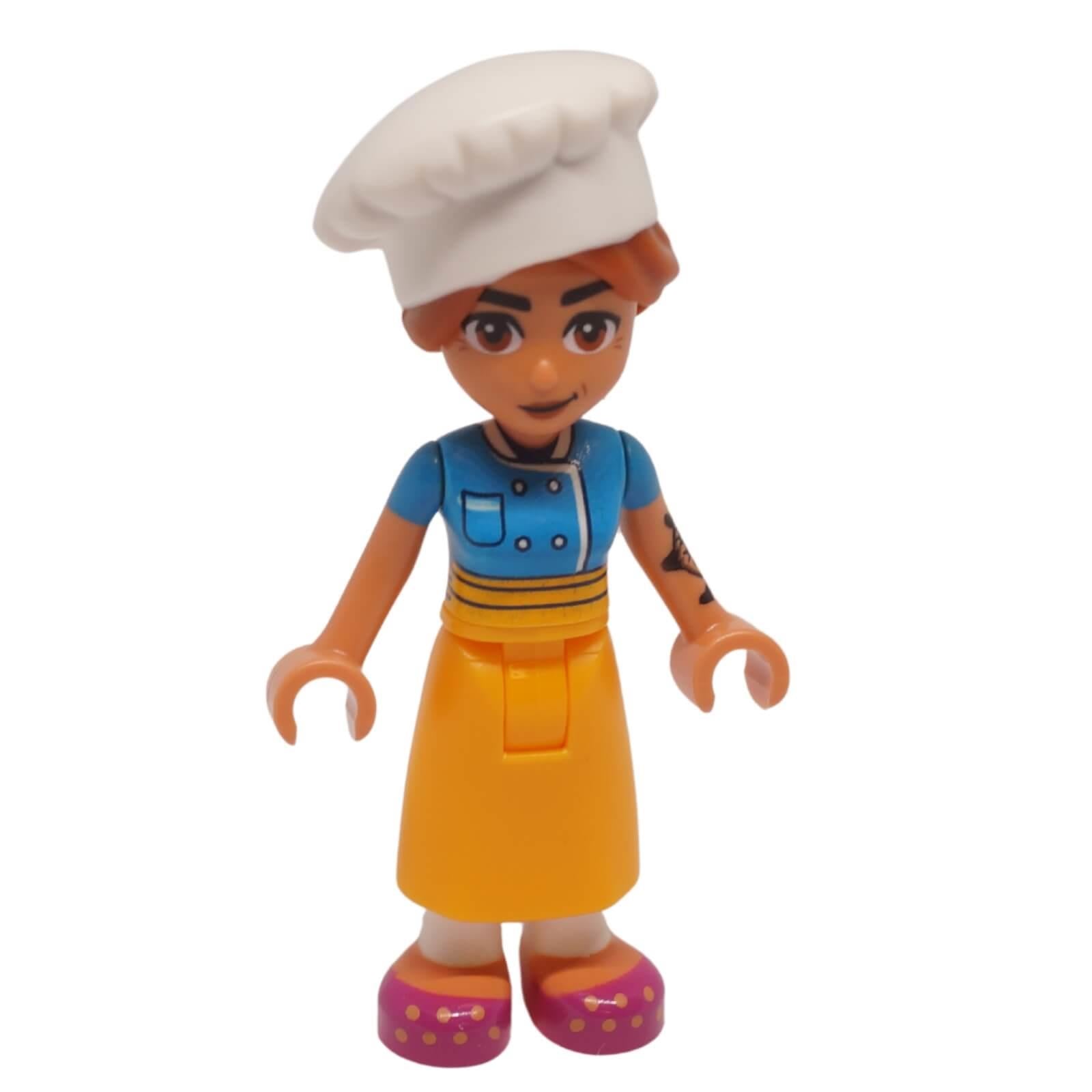 Vista frontal de la minimuñeca de Chef Marta Friends con gorro de chef blanco, camisa de chef azul y falda naranja
