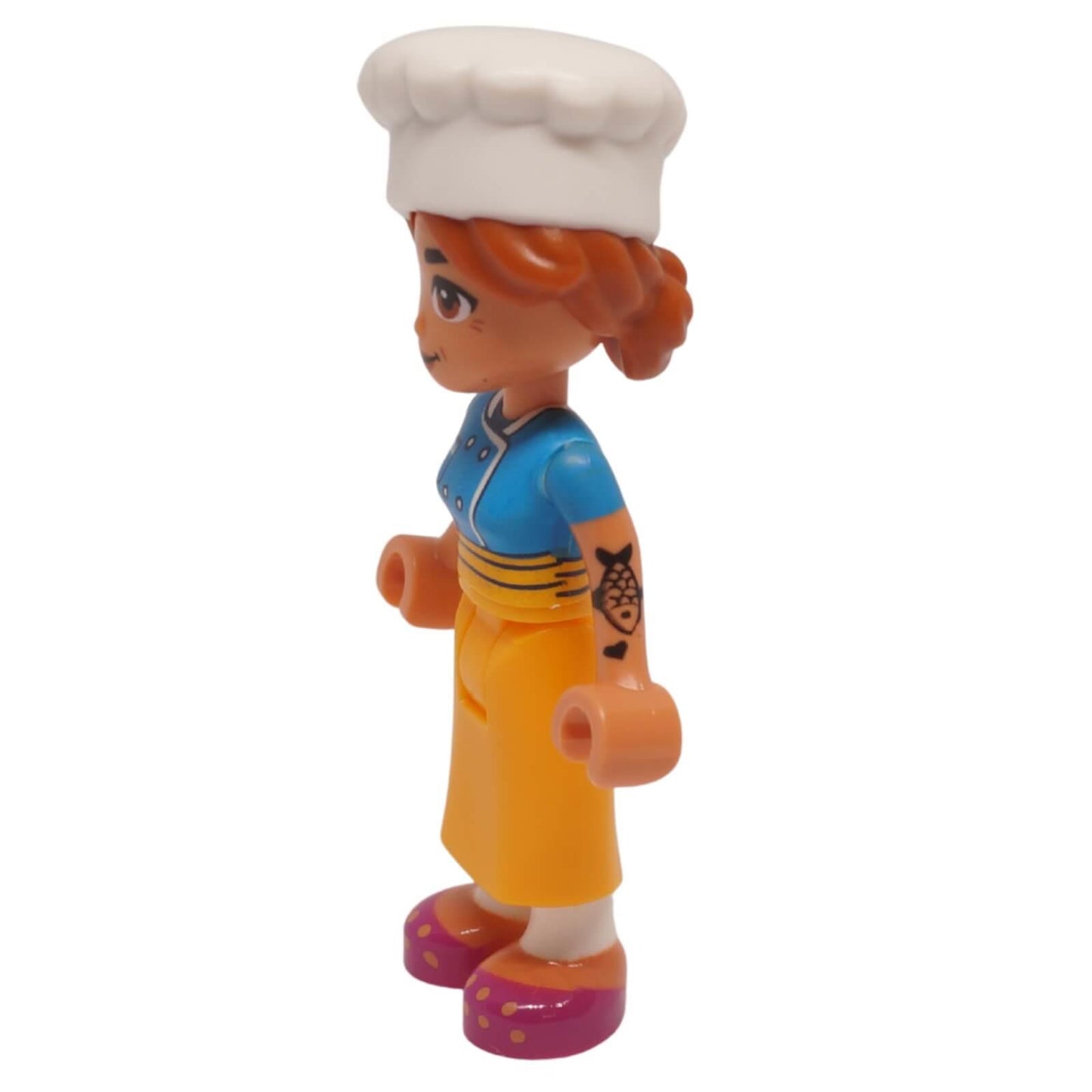 Vista lateral de la minimuñeca de Chef Marta Friends con gorro de chef blanco, top azul y falda naranja
