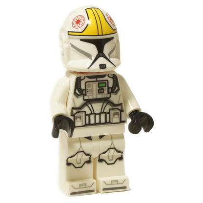 A LEGO® Star Wars™ Phase 1 Clone Trooper Pilot -minihahmo, jolla on nougat-päinen vakava ilme, päällä valkoinen haarniska, jossa on mustaa, harmaata ja vihreää rintapainatusta, valkoiset käsivarret, mustat kädet ja valkoiset jalat, joissa on mustaa ja harmaata haarniskapainatusta. Erillinen valkoinen Phase 1 pilotin kypärä, jossa on keltaiset raidat ja punainen tasavallan symboli, on asetettu minihahmon viereen, kaikki valkoista taustaa vasten.