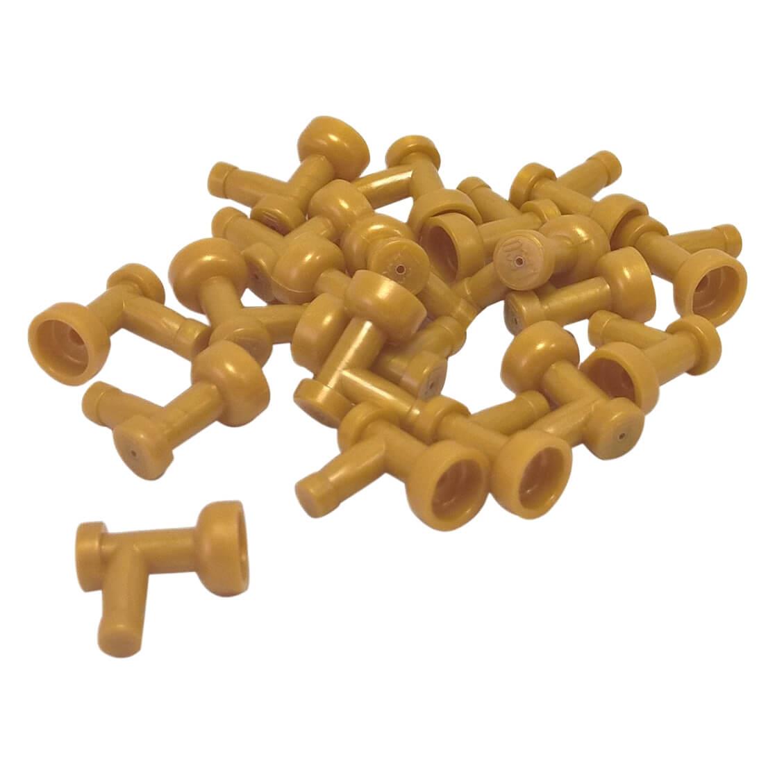 A pile of numerous pearl gold LEGO Part 4599b (Tap 1 x 1 without Hole in End) pieces scattered against a white background, showing their T-shape with a flared cup end.