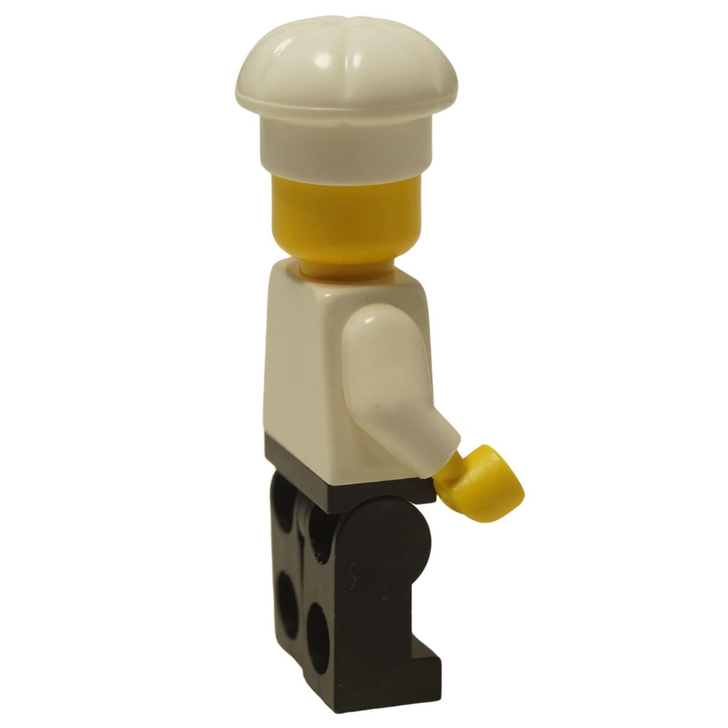 LEGO® Klasická minifigurka kuchaře (chef002) s typickým úsměvem, oblečená v bílém uniformě s černými nohavicemi a vysokou kuchařskou čepicí. Pohled z boku.