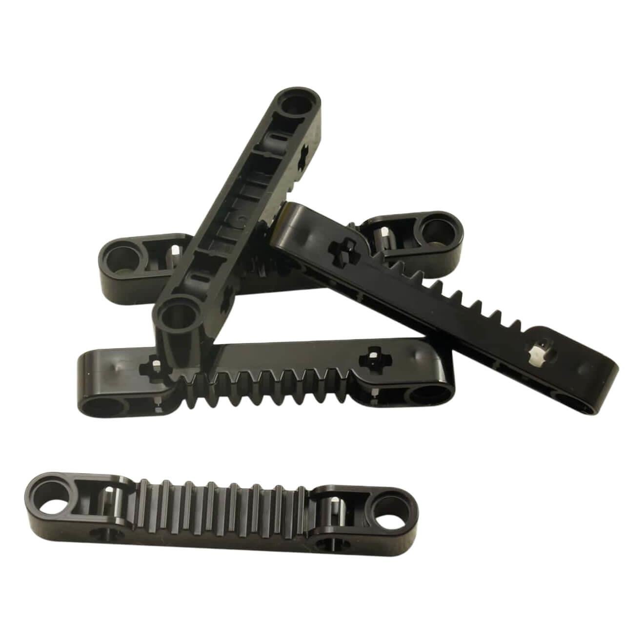 A pile of five black LEGO Technic Gear Rack 1x7 pieces (8776) showing their ridged, ratcheting edges.
